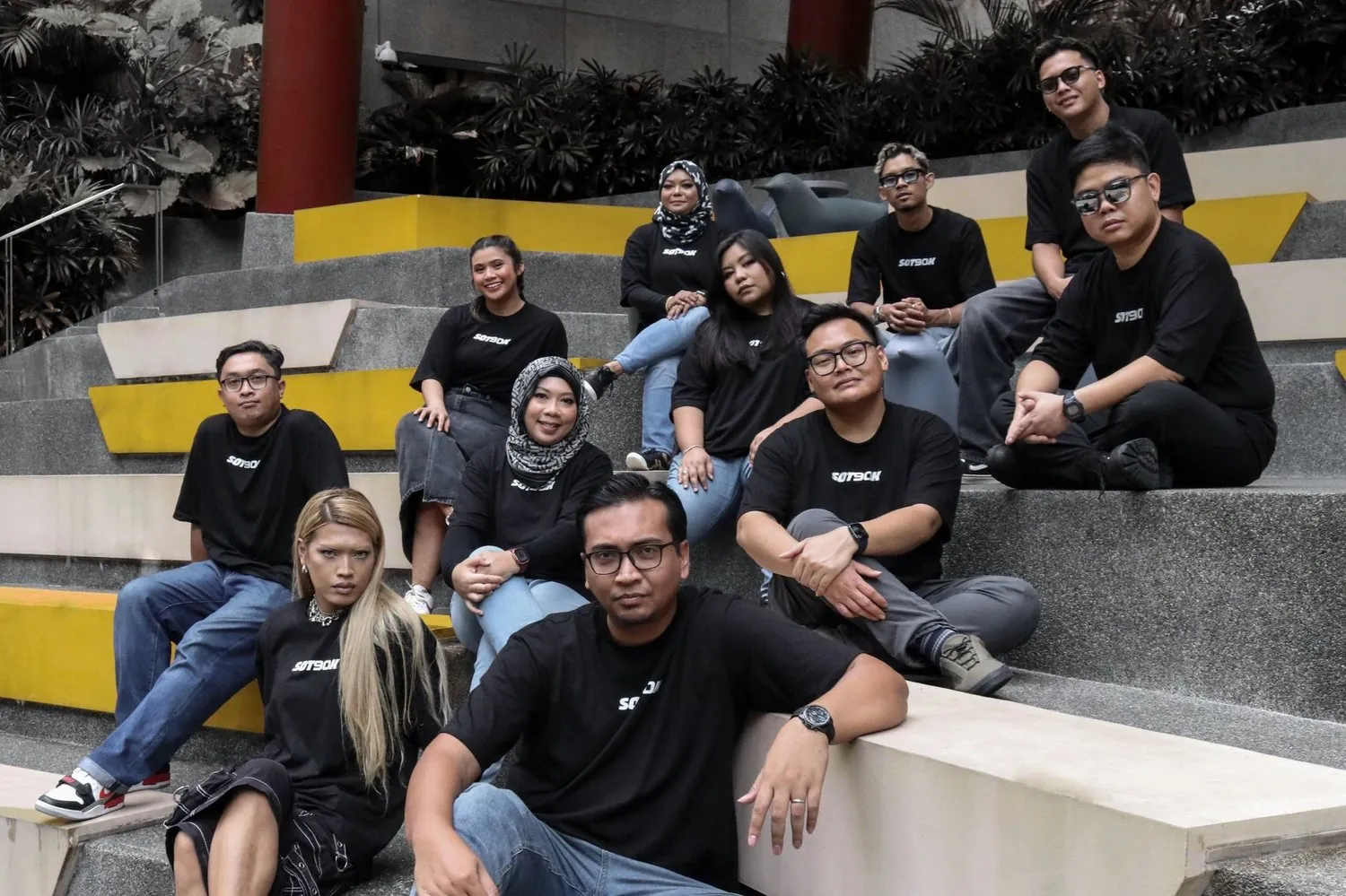 The eleven SOT90K partners sitting on yellow and grey steps in matching black SOT90K tees